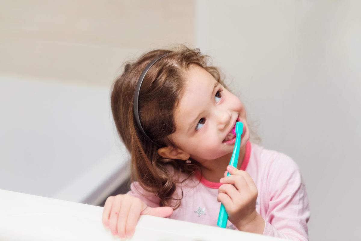 Little girl in pink pyjamas in bathroom brushing teeth